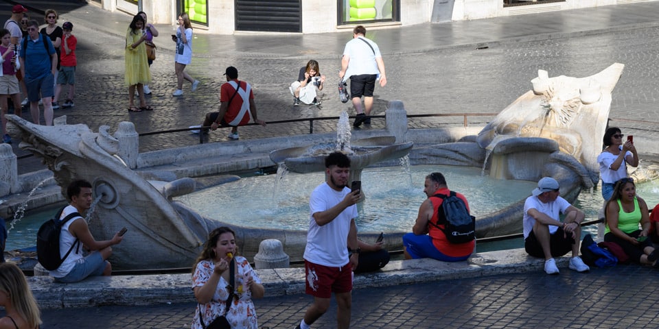 Los turistas se relajan y toman fotos junto a la Fuente de la Barcaccia en Roma.