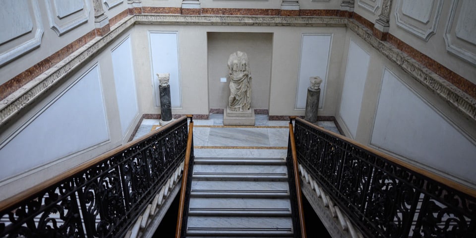 Marble staircase with wrought-iron railing and an ancient statue in the National Roman Museum, Baths of Diocletian, Rome