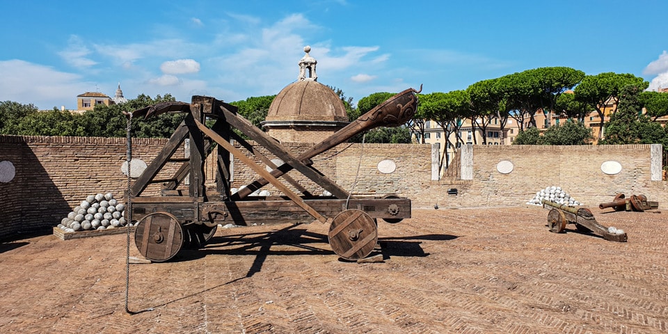 Reconstructed catapult and stacked stone cannonballs on the ramparts of Castel Sant'Angelo with the dome of St. Peter's behind, Rome